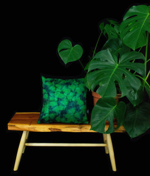 Forest Explorer cushion displayed on wooden table next to a cheeseplant and black backdrop